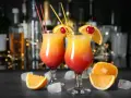 Dwa drinki Malibu z sokiem pomarańczowym, ozdobione pomarańczą i wiśnią, na tle baru.