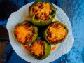Cuatro pimientos verdes rellenos con carne, frijoles y arroz, cubiertos con queso derretido, servidos en un plato blanco.