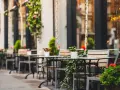 Mesas y sillas vacías en la terraza de un restaurante, adornadas con plantas y flores. Un lugar acogedor, listo para recibir clientes tras obtener las licencias de restaurantes.