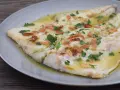 Pescado blanco cocinado en aceite con ajo laminado y perejil picado, servido en plato gris.