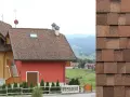 Domy z brązowym dachem, gdzie widoczne jest układanie papy na zimno. W tle krajobraz z pagórkami.