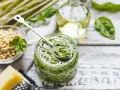 Un barattolo pieno di profumato pesto alla genovese, con pinoli, basilico e olio d'oliva pronti per essere mescolati.