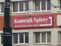 Tablica "Komornik Sądowy" na budynku. Wskazuje wejście z drugiej strony.