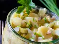 Ein köstlicher Kartoffelsalat ohne Mayo, mit Gurken und frischen Kräutern, serviert in einem Glas.