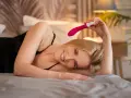 Uśmiechnięta blondynka leży na łóżku z różowym masażerem. Pytanie, ile trwa leczenie onanizmu, nie ma tu zastosowania.