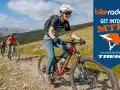 Three friends enjoy a sunny day of cross country biking on a rocky mountain trail, with a "Get Into MTB" logo in the corner.