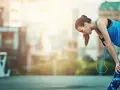 Atleta esausta appoggiata a un corrimano, con le cuffie. Potrebbe aver bisogno di rimedi per il sovrallenamento.