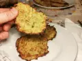 Una mano tiene una frittella di zucchine dorata e croccante. Sul piatto, altre frittelle di zucchine invitano ad essere gustate.