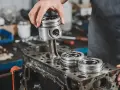 Mechanik montuje tłok do bloku silnika. Na bloku leżą inne tłoki.
