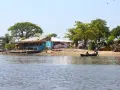 Nad rzeką w Gambii, przy brzegu z łodziami i budynkami, widać tablicę "Welcome to THE GAMBIA".