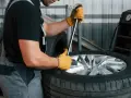 Mechanik w żółtych rękawiczkach używa klucza do odkręcania śrub, pokazując, jak ściągnąć oponę z felgi.