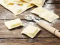 Świeże włoskie pierożki ravioli, różne rodzaje, gotowe do gotowania. Obok kółko do ciasta.