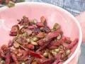 Un plato rosa lleno de habas con jamón, guisantes y un chile rojo seco.