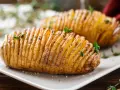 Patate hasselback dorate e croccanti, appena sfornate dalla friggitrice ad aria, guarnite con erbe aromatiche fresche.