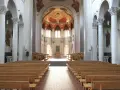 Interior of a grand abbey, with rows of wooden pews leading to an altar. The domed ceiling features a vibrant fresco. Check the abbey mass schedule for service times.