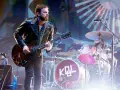 Gitarzysta Kings of Leon Polska w skórzanej kurtce gra na scenie. W tle perkusja z logo KQL.