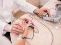 Lekarz wykonuje próbę tężyczkową, podłączając elektrody do dłoni pacjenta i regulując aparat.
