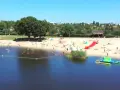 Słoneczny dzień nad jeziorem Grzymisławskim. Ludzie odpoczywają na plaży, kąpią się i bawią na dmuchanych atrakcjach.
