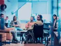Ein Team bespricht sich, eine Frau im Rollstuhl ist integriert. Ein leidensgerechter Arbeitsplatz, an dem alle willkommen sind.