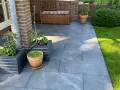 Moderne Terrassenplatten grenzen an einen gepflegten Rasen. Pflanzen in Töpfen und ein Holzbänkchen bieten schöne Rasenkante Ideen.