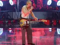 Krzysztof Zalewski na koncercie, śpiewa i gra na gitarze. Scena oświetlona czerwonymi światłami.
