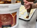 Un repostero decora galletas con una manga pastelera, usando el delicioso dulce de leche de un gran envase.