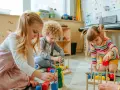 Drei Kinder, darunter ein **kind 8 jahre**, spielen konzentriert mit bunten Holzbausteinen im Kindergarten.
