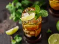 Szklanka z drinkiem Cuba Libre, lodem, plasterkami limonki i miętą.