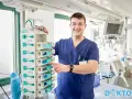 Uśmiechnięty anestezjolog, kto to? Lekarz dbający o bezpieczeństwo pacjenta podczas zabiegu, kontroluje aparaturę medyczną.