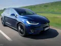 Granatowy Tesla Model X w ruchu na drodze, z widocznym kierowcą.
