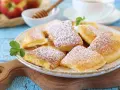 Puszysty omlet z jabłkiem, posypany cukrem pudrem, na talerzu z listkiem mięty. Obok jabłka i miód.