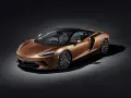 Elegancki, miedziany McLaren GT z czarnym dachem i felgami, prezentujący swoje sportowe linie na ciemnym tle.