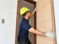 Pracownik w żółtym kasku montuje nowe drzwi na stare futryny.