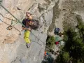 Frau klettert in Briançon, gesichert durch ein Seil. Unten warten Freunde mit Ausrüstung.