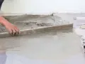 Ręka robotnika wyrównuje świeżą szlichtę budowlaną za pomocą łaty.
