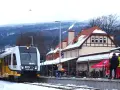 Pociąg GRYFC na stacji w Świeradowie-Zdroju, zimowy krajobraz z ośnieżonymi górami w tle.