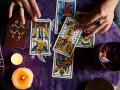 Manos de tarotista que es, barajando cartas y velas encendidas sobre tela morada.