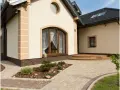 Elewacja domu kostka w jasnym kolorze, z ozdobnymi elementami i brązową cegłą u podstawy.