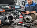 Mechanik trzyma mocno zabrudzony zawór EGR. Obok leżą turbosprężarka i narzędzia.