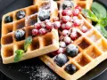 Keto gofry z mąki kokosowej z borówkami, porzeczkami i miętą, posypane cukrem pudrem.