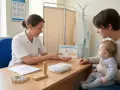 Pielęgniarka omawia zdrowie i szczepienia z rodzicem, który trzyma na rękach niemowlaka.