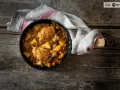 Estofado de pollo con patatas y zanahorias en sartén sobre mesa de madera.