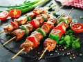 Spiedini di carne succulenti con peperoni e cipolle, pronti per essere gustati con una salsa rossa e pomodorini freschi.