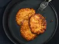 Drei goldbraune Kartoffelpuffer, frisch zubereitet im Thermomix, liegen auf einem dunklen Teller.