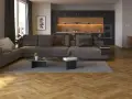 Nowoczesny salon z szarą kanapą i czarną ścianą w tle. Drewniana podłoga w jodełkę dodaje ciepła.
