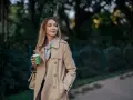 Donna con trench beige, un classico del marchio Burberry, sorseggia un caffè all'aperto.
