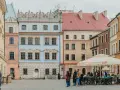Kolorowe kamienice na rynku, idealne na tani city break. Ludzie spacerują, siedzą w ogródku kawiarnianym.