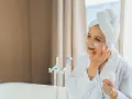 Kobieta w szlafroku i ręczniku na głowie aplikuje krem pod oczy. Witamina A pod oczy to klucz do odmłodzenia skóry.