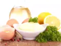 Un bol de mayonnaise maison crémeuse, entouré d'œufs, de citron, d'huile et de persil.
