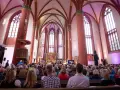 Menschen sitzen in einer Kirche, die für eine Veranstaltung beleuchtet ist. Es ist schön, dass man wieder in die Kirche eintreten kann.